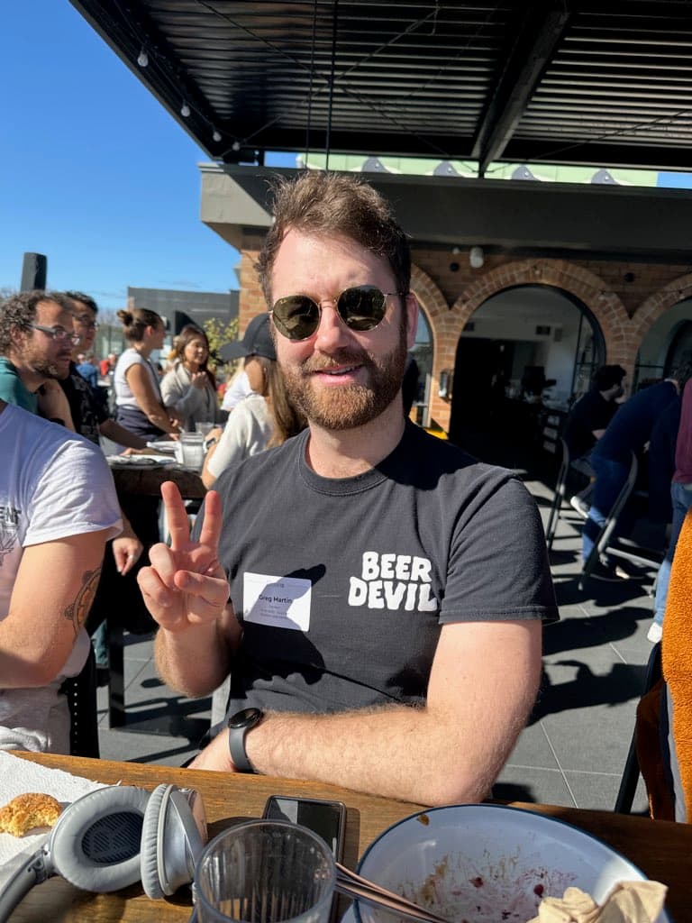 Greg sitting on the sunny Canva rooftop eating a cookie giving the peace sign