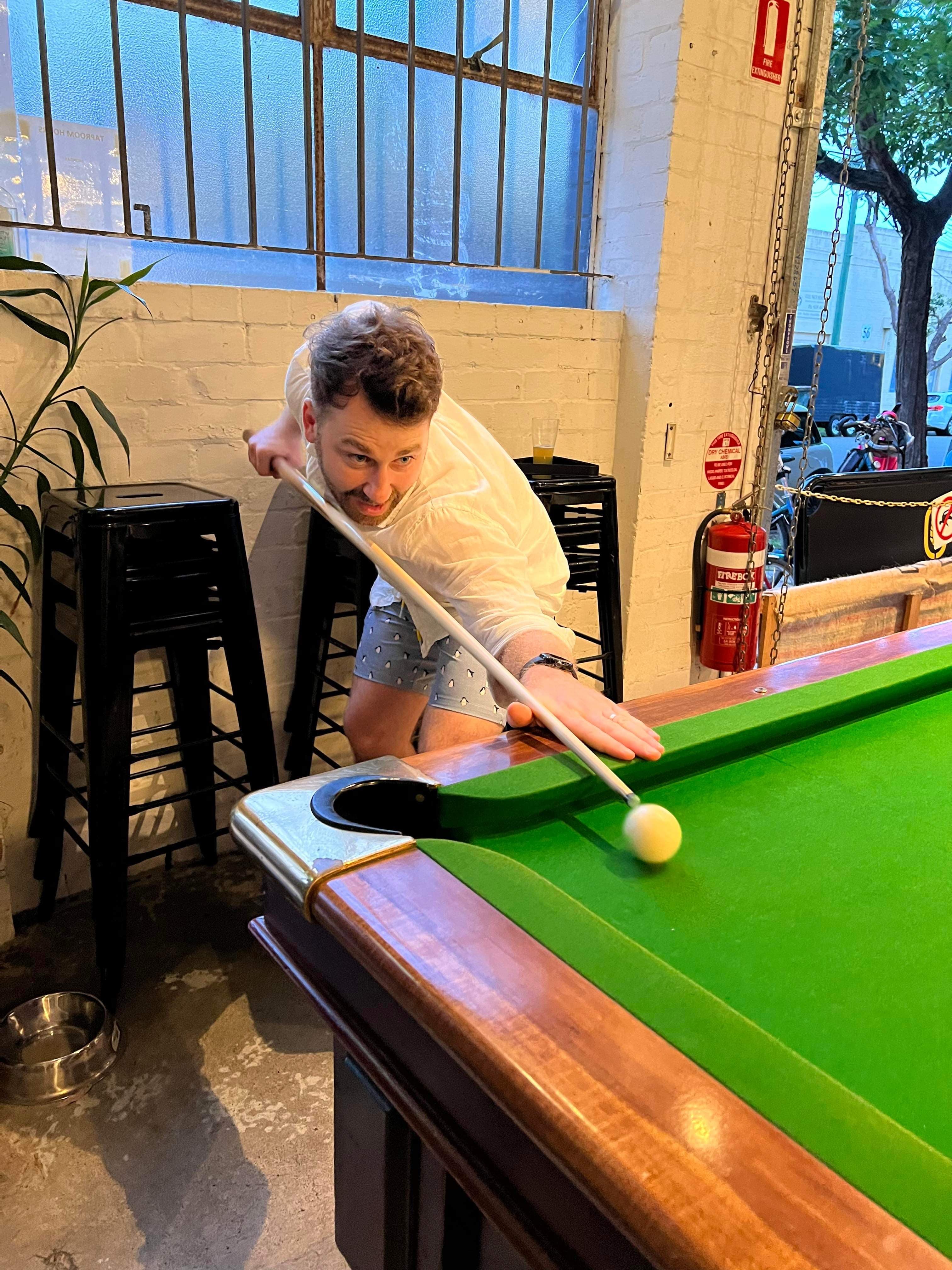 Greg playing pool, leaning over the table to take a shot.